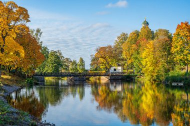 İsveç 'ten güzel bir sonbahar manzarası. Bir köprü var. Etrafı canlı sonbahar ağaçları ve arka planda bir kilise kulesi ile çevrili.