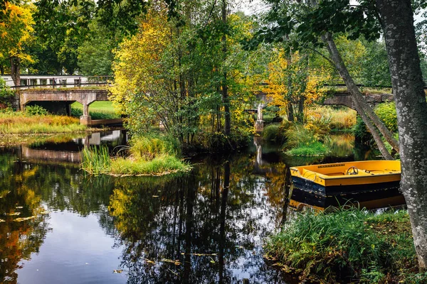 秋天美丽的景色 一条狭窄的河流 有一座过桥和一艘停泊的黄色小船 — 图库照片