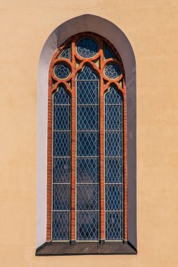 Kayısı rengi bir duvarda, kurşunlu süslemeler ve tuğlalı pencere parmaklıkları olan güzel bir kilise penceresinin detaylı görüntüsü.