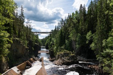 İsveç 'te her iki tarafında yeşil orman ve akan bir nehir olan bir dere. Yüksek bir demiryolu köprüsü kanyonu geçiyor.