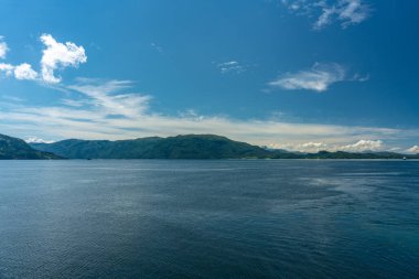 Güzel manzara manzarası Norveç 'te bir fiyort ya da körfezi geçiyor. Açık mavi gökyüzü, güneş ışığı ve arka planda dağlar var.