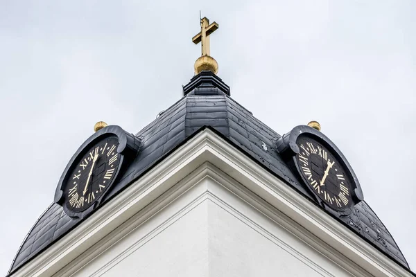 Close view of a white church tower with dual clock faces and golden dials against a white sky