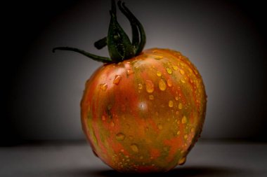 Turuncu ve altın renkli domateslerin yakın çekimi. Su damlaları ve koyu arkaplan ile aydınlatılmış