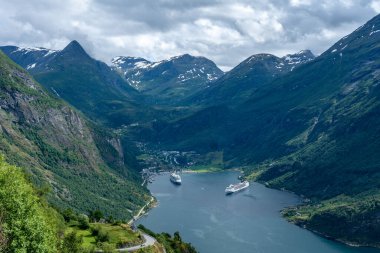 Geiranger, Norveç, 2016-07-06. Yaz mevsiminde Geiranger Vadisi ve fiyort dik yeşil dağ yamaçları ve körfeze demir atmış iki büyük gemi.