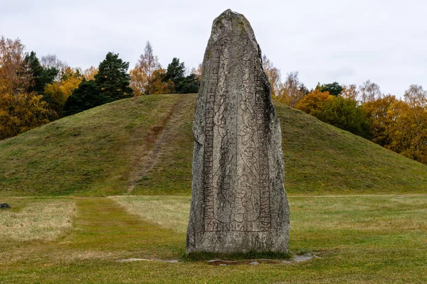1200 yaşında İsveç 'in Anundshog şehrinde bulunan çok büyük bir rün taşı. Arka planda sonbahar renkli ağaçlar var.