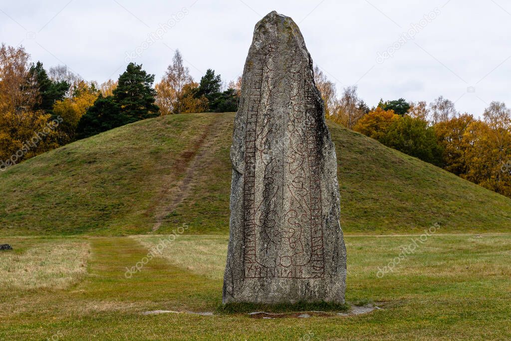 Twelve hundred year old very and very large rune stone located at Anundshog in Sweden, with autumn colored trees in the background
