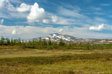 İsveç 'in kuzeyindeki, neredeyse Norveç sınırına kadar uzanan, karla kaplı bir dağın güzel manzarası. Mavi gökyüzü ve yumuşak beyaz bulutlarla