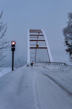 Kuzey İsveç 'te karlı bir nehirden geçen kırmızı ışık kontrollü tek şeritli asma köprü ve diğer taraftan geçen bir araba..