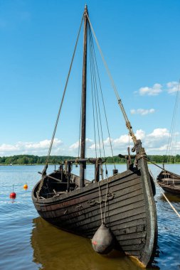 Tahtadan yapılmış eski siyah bir tekne, güzel yaz güneşinde limana demirlemiş.