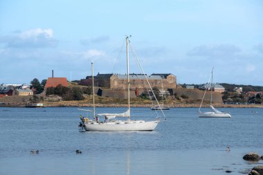 İsveç 'in Varberg adasının dışındaki takımadalarda yelkenlilerin güneşli manzarası, arka planda büyük eski bir kale var.
