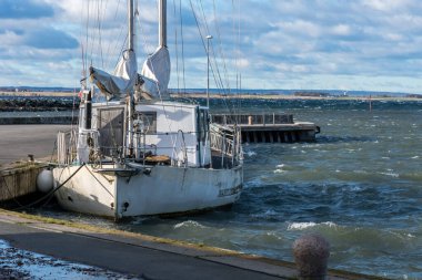 Limanda demirli eski beyaz yelkenli, denizden gelen dalgalar yüzünden suda sallanıyor.