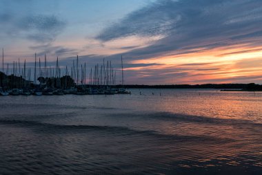 İsveç 'in doğu kıyısındaki küçük bir tekne limanında demirlemiş yelkenli tekneler, direkleri ve çizgileri güzel pembe, orannge ve mavi akşam gökyüzüne karşı..