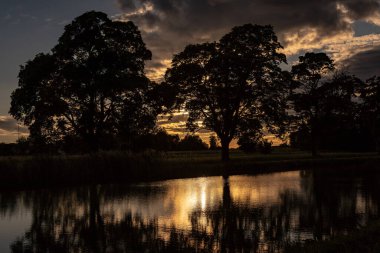 İsveç 'te bir nehrin kenarında güzel bir gün batımı, karanlık siluetler ve suyun kenarında duran ağaçların yansımaları.