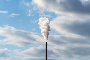 Tek bir baca bacası gökyüzünde yükseliyor, kirliliği havaya uçuruyor. Gri bulutlu mavi gökyüzüne karşı