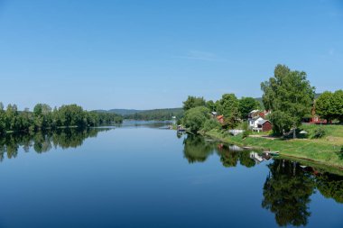 İsveç 'te nehir kenarındaki küçük yazlıklar güzel bir yaz gününde mavi gökyüzü ve sakin bir su aynası gibi.
