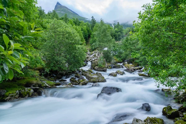 素晴らしいノルウェーの山々からの風景 緑豊かな緑の木々と背景の山のピークと山の中腹に流れる白い柔らかい水を流れる小川 — ストック写真