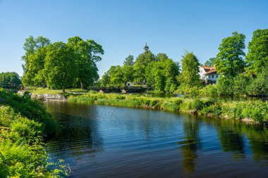 Stromsholms kanalı, bereketli yeşil ağaçlar ve mavi gökyüzü ile güzel yaz güneşinde kayık şeridine ve elektrik santraline saptı. Bazı çocuklar banyo yapıyor ve köprüden atlıyor.