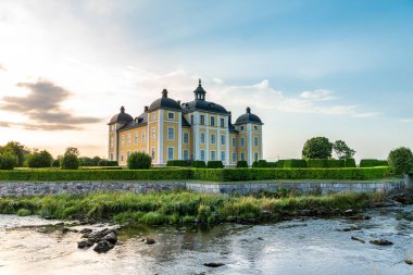 İsveç şatosu Stromsholm 'un güzel bir yaz öğleden sonrası manzarası. Çevresi yeşil şekilli kesim çitlerle çevrili ve Stromsholms kanalı dışarıda geçiyor..