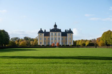 İsveç 'teki güzel sarı Stromsholm şatosu. Etrafında sonbahar renkli ağaçlar ve akşam güneşi var.