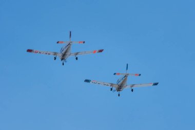 İki okul pervanesi birbirine yakın uçuyor. Bir kırmızı ve bir mavi açık mavi gökyüzüne karşı