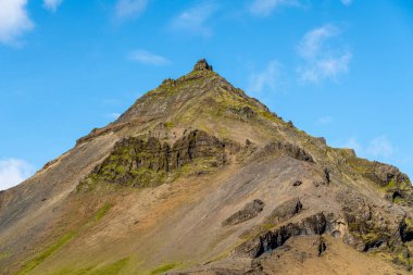 İzlanda 'daki aşınmış volkanik dağ zirvesi, mavi gökyüzünde yükseliyor.