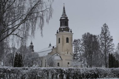 Kışın siyah saat kulesi olan beyaz taş kilise, karlı ve buzlu ağaçlarla çevrili.