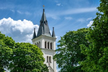 Mavi gökyüzüne ve çevresini çevreleyen yeşil ağaçlara karşı beyaz bir kilise kulesinin güzel manzarası.