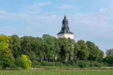 İsveç kırsalında, yemyeşil ağaçlar ve mavi gökyüzü ile çevrili güzel bir kilise kulesi manzarası.