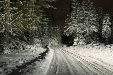 Gece bir kış yolunda araba sürerken, yoldaki kar ve buz parlak bir ışık saçar.