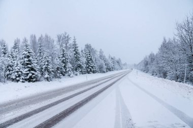 İsveç kırsalında kaygan bir kış yolu manzarası var, güneş parlıyor. Ağaçlardan kar ve buz sarkıyor..