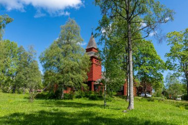 Kırmızıya boyanmış eski ahşap bir kilisenin İsveç kırsalında güzel bir yaz manzarası. Yaz güneşi altında yemyeşil ağaçlarla çevrili.