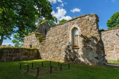 Eski bir ortaçağ kilisesinin güzel yaz manzarası. Önünde eski bir mezar, parlak güneş ışığı, yemyeşil ağaçlar ve mavi gökyüzü.