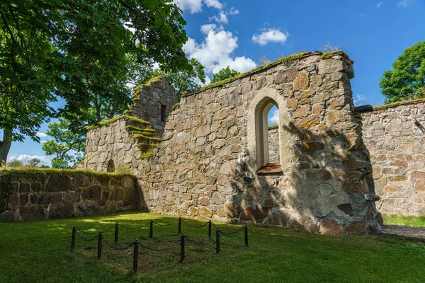 Eski bir ortaçağ kilisesinin güzel yaz manzarası. Önünde eski bir mezar, parlak güneş ışığı, yemyeşil ağaçlar ve mavi gökyüzü.
