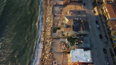 Güney Kaliforniya 'da okyanus kıyısında deniz manzaralı 4K hava aracı görüntüsü. Dalgalar geliyor ve güzel günbatımında güzel evleri olan mavi Pasifik Okyanusu.