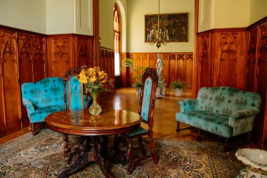 Lednice, Güney Moravya, Çek Cumhuriyeti, 04 Temmuz 2021: Neo-gotik ahşap oymalı tavan ve mobilya, sandalye ve kanepeli masa, vazoda bir buket sarı çiçek.