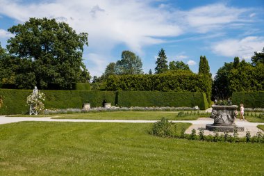 Lednice, Güney Moravya, Çek Cumhuriyeti, 04 Temmuz 2021: Güzel bahçeli şato, güneşli yaz gününde yeşil parklar, neo-gotik romantik kale, geometrik çiçek yatağı, güller ve taş vazo.