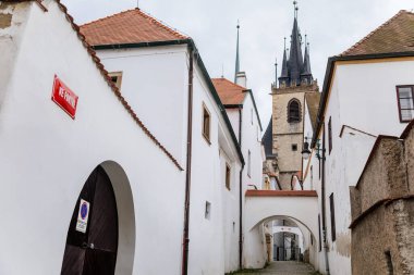 Louny, Çek Cumhuriyeti, 19 Eylül 2021: Ortaçağ şehrinin tarihi merkezinde dar resim caddesi, sonbahar günü St. Nicholas Kilisesi 'nin gotik kulesi, beyaz kasaba binaları, kemerli geçit