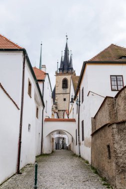 Louny, Çek Cumhuriyeti, 19 Eylül 2021: Ortaçağ şehrinin tarihi merkezinde dar resim caddesi, sonbahar günü St. Nicholas Kilisesi 'nin gotik kulesi, beyaz kasaba binaları, kemerli geçit