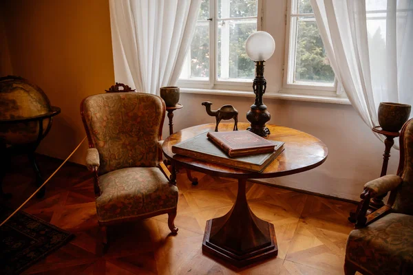 Libochovice, Bohemya, Çek Cumhuriyeti, 19 Eylül 2021: Barok ahşap mobilya, kütüphane, masa ve sandalyenin karşısındaki pencere, iki büyük antika kitap, lamba ve deve heykeli