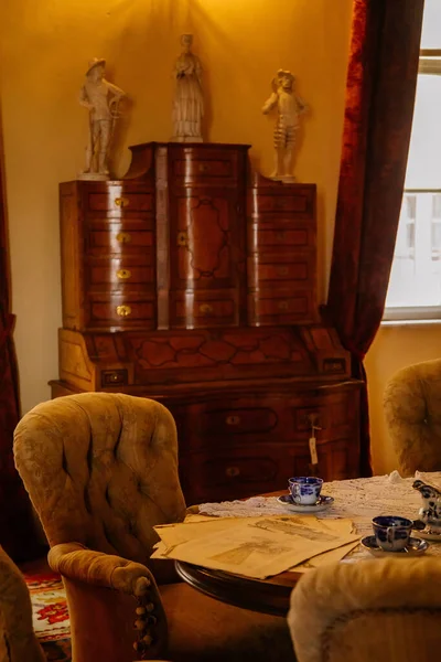 Libochovice, Bohemya, Çek Cumhuriyeti, 19 Eylül 2021: Barok ahşap mobilyalar, kolay sandalye, porselen kahve fincanı masa ve antika gazete, arka plandaki çekmeceler