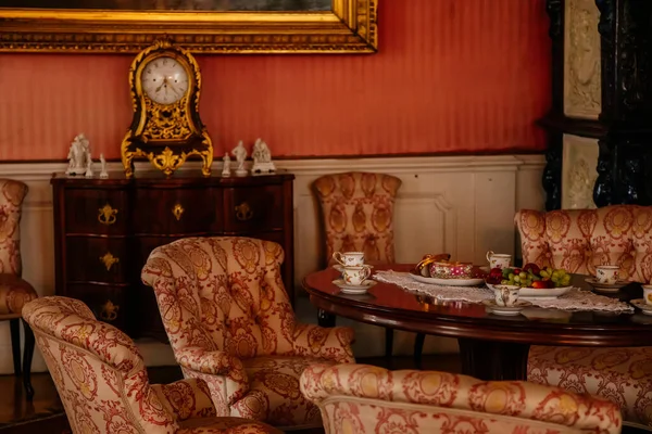 Libochovice, Bohemya, Çek Cumhuriyeti, 19 Eylül 2021: Barok oymalı mobilyalar, kanepesi ve koltuğu olan misafir salonu, masada porselen çay seti, şifoniyerde klasik yaldızlı saat