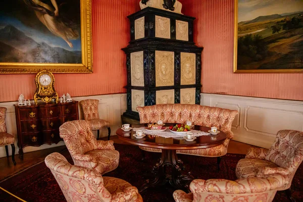 Libochovice, Bohemya, Çek Cumhuriyeti, 19 Eylül 2021: Barok ahşap oymalı mobilya ile kale iç mimarisi, seramik seramik döşemeli ocak yanında koltuk ve koltukları olan misafir salonu, masa başında porselen çay seti