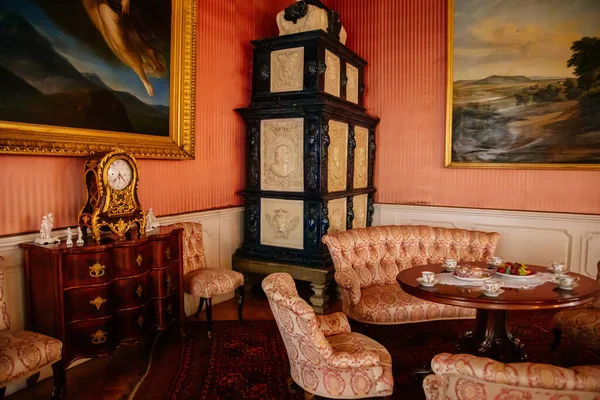 Libochovice, Bohemya, Çek Cumhuriyeti, 19 Eylül 2021: Barok ahşap oymalı mobilya ile kale iç mimarisi, seramik seramik döşemeli ocak yanında koltuk ve koltukları olan misafir salonu, masa başında porselen çay seti