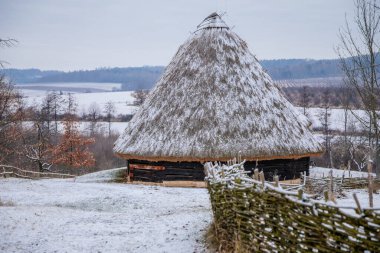Kourim, Czech Republic, 26 December 2021: Traditional village wooden timbered barn with low walls and steep thatched roof in winter, historic country-style architecture, open-air ethnographic museum