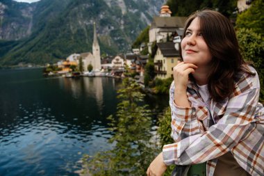 Hallstatt, Avusturya: Güzel, romantik, genç bir kadının portresi turist gülümsemesi, doğal ışık, vücut pozitifliği, bej renkli, beyaz çizgili bir kız, manzara manzaralı bir kasaba caddesi.