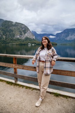 Hallstatt, Avusturya: Güzel, romantik, genç bir kadının portresi turist gülümsemesi, doğal ışık, vücut pozitifliği, bej renkli, beyaz çizgili bir kız, manzara manzaralı bir kasaba caddesi.