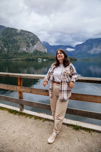 Hallstatt, Avusturya: Güzel, romantik, genç bir kadının portresi turist gülümsemesi, doğal ışık, vücut pozitifliği, bej renkli, beyaz çizgili bir kız, manzara manzaralı bir kasaba caddesi.