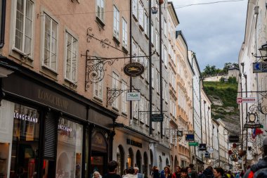Salzburg, Avusturya, 28 Ağustos 2021: Tarihi Altstadt veya Eski Şehir 'de bulunan ünlü Getreidegasse alışveriş dar caddesi, yaz günü demir lonca tabelaları astı, çok sayıda yüksek konak evi gökyüzüne yükseldi