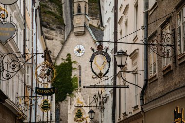 Salzburg, Avusturya, 28 Ağustos 2021: Tarihi Altstadt veya Eski Şehir 'de bulunan ünlü Getreidegasse alışveriş dar caddesi, yaz günü demir lonca tabelaları astı, çok sayıda yüksek konak evi gökyüzüne yükseldi