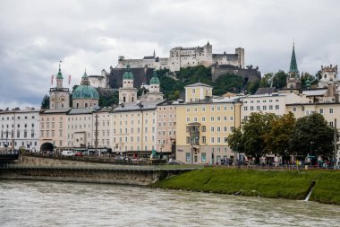 Salzburg, Avusturya, 28 Ağustos 2021: Tepedeki eski ortaçağ kalesi, Hohensalzburg Kalesi, Salzach nehrinin seddi, Rönesans ve barok evleri, yaz günü taş bina cephesi
